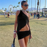 A woman with sunglasses and a choker necklace poses in a black one-shoulder top and mini skirt at an outdoor festival.