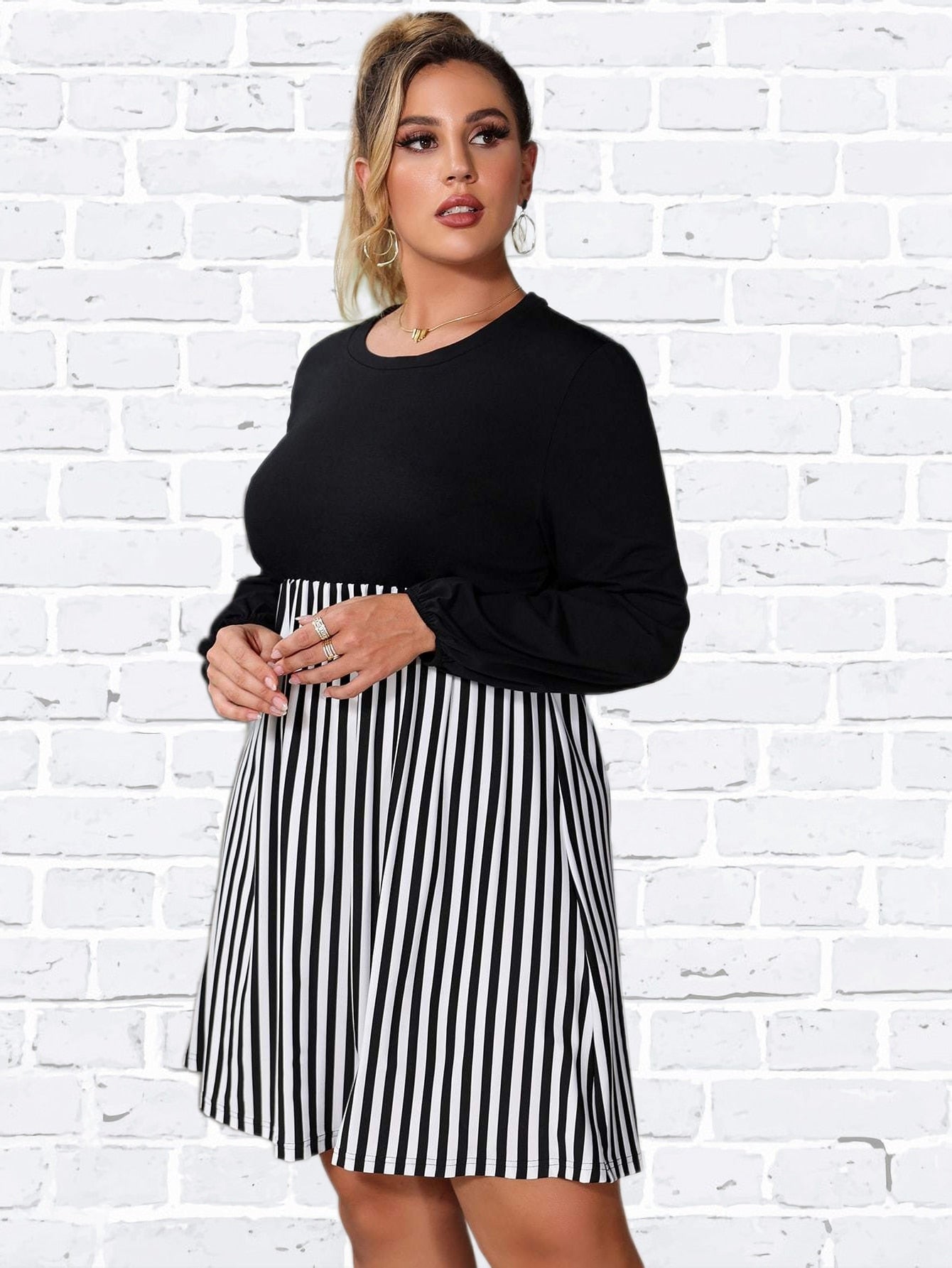 Woman wearing a black and white striped dress, with hands clasped in front.