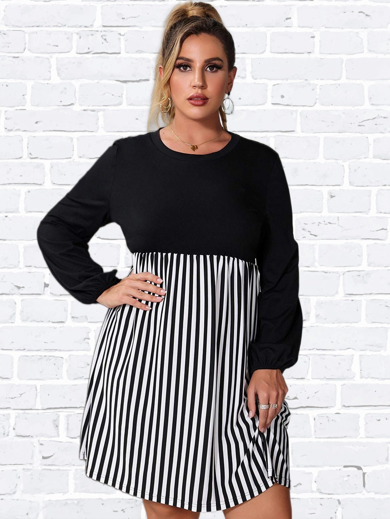 Woman wearing a black and white striped dress, posing with one hand on her hip.