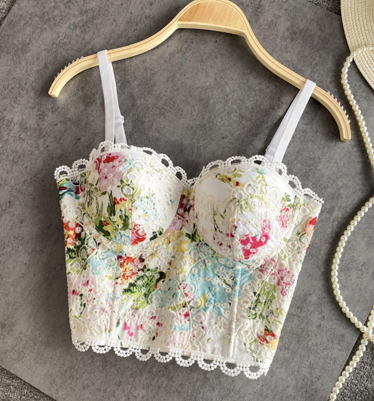 A white floral print corset top with lace trim hanging on a wooden hanger.