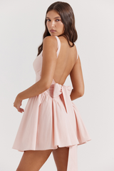 Model wearing a pink mini dress with a square neckline and a large bow detail on the back.