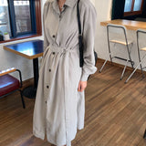 Full shot of a woman in a gray midi dress with a belt and black crossbody bag.