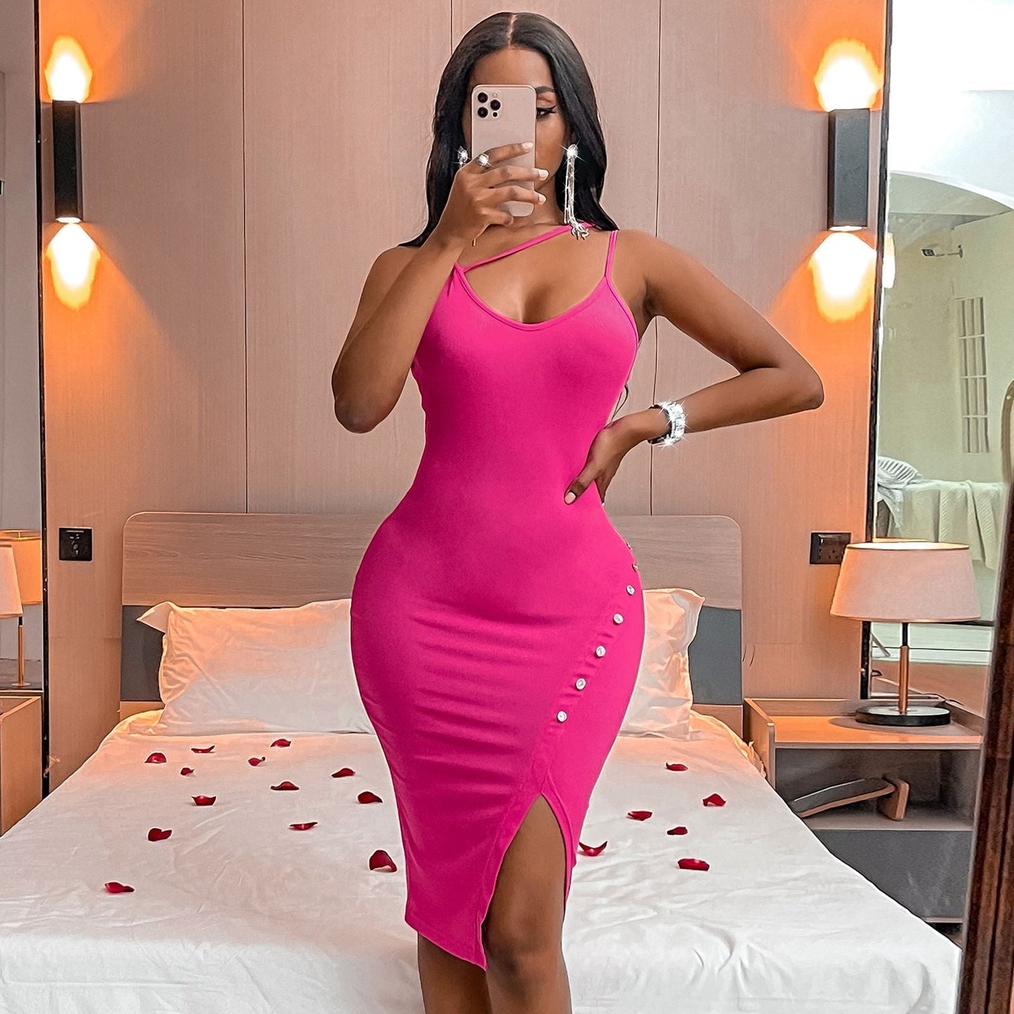 Woman in a pink bodycon dress with an asymmetrical neckline and a high slit, taking a mirror selfie.