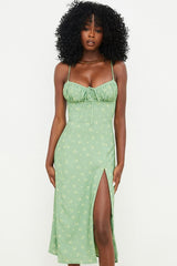 A Black woman poses in a light green floral print midi dress with spaghetti straps and a thigh-high slit.