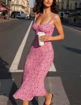 Woman in a pink floral midi dress walking across a street with a coffee cup