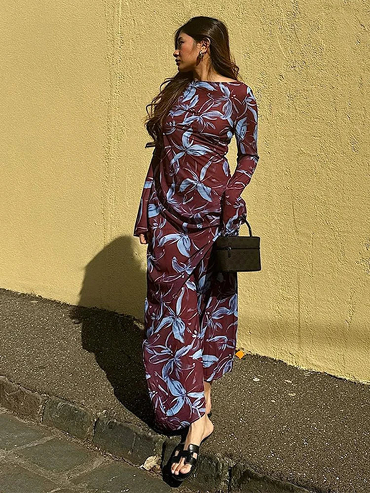 Woman in a burgundy and blue floral print maxi dress, standing against a yellow wall.