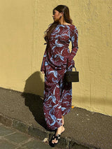 Woman in a burgundy and blue floral print maxi dress, standing against a yellow wall.