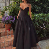 Woman in a black satin strapless dress with a full skirt, standing in a garden.