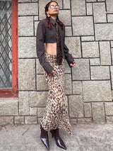 A woman wearing a brown cropped shirt, tie, and a long leopard print skirt.