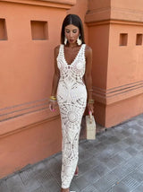 Woman in a white crochet maxi dress standing against an orange wall.