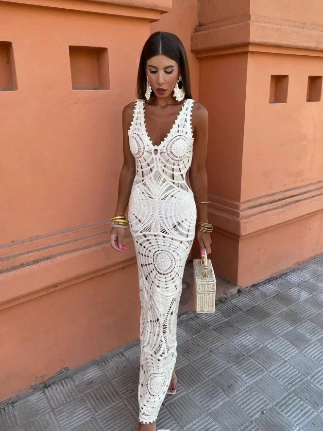 Woman in a white crochet maxi dress standing against an orange wall.