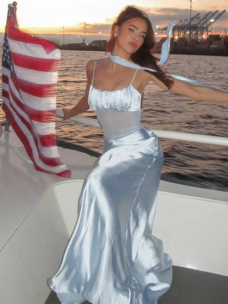 Woman in a light blue satin slip dress with a ruched bust and sheer midsection, standing on a boat with an American flag.