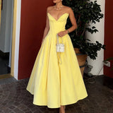 Woman in a yellow satin strapless dress with a full skirt, holding a small white purse.