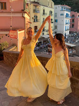Two women in yellow dresses holding hands and smiling in front of a town and ocean