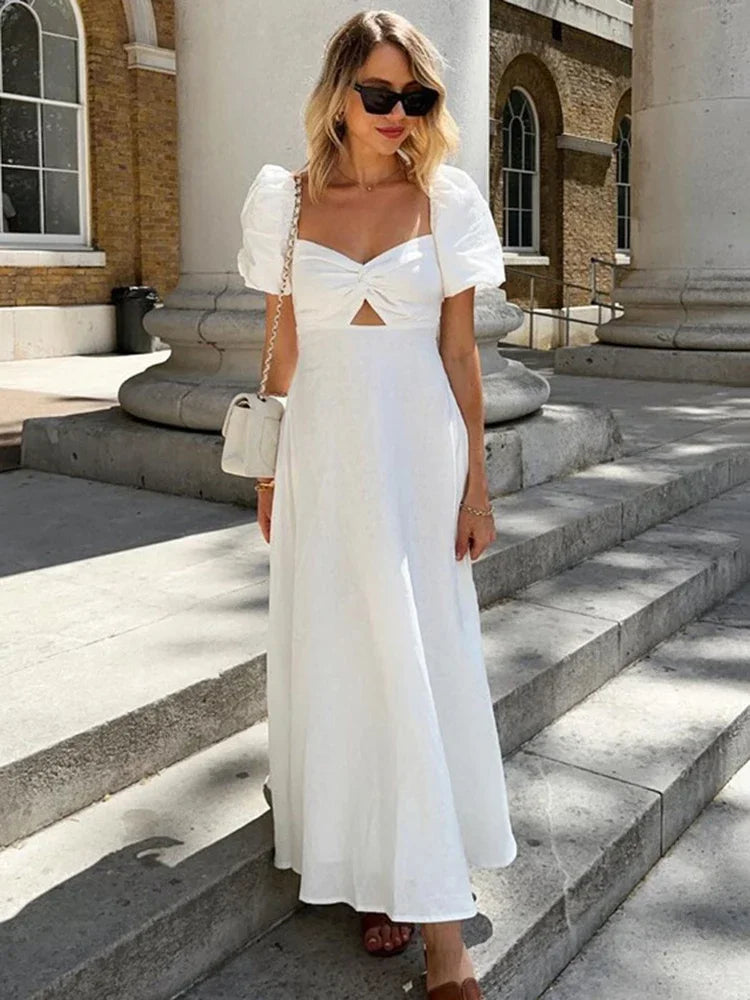 Woman wearing a white puff sleeve midi dress with a cut-out detail and twist front bodice, standing on stone steps outdoors.
