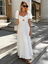 Woman wearing a white puff sleeve midi dress with a cut-out detail and twist front bodice, standing on stone steps outdoors.