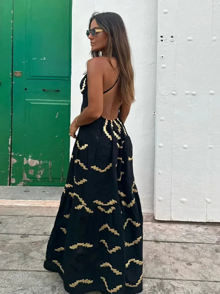 Woman in a black maxi dress with a gold geometric print, standing with her back to the camera.