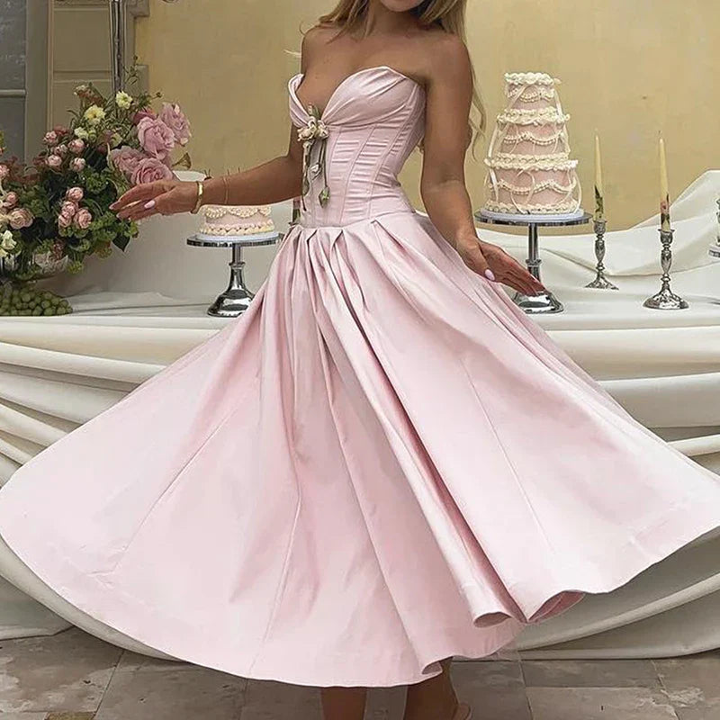 Woman in a pink satin strapless dress with a full skirt, standing in front of a cake display.