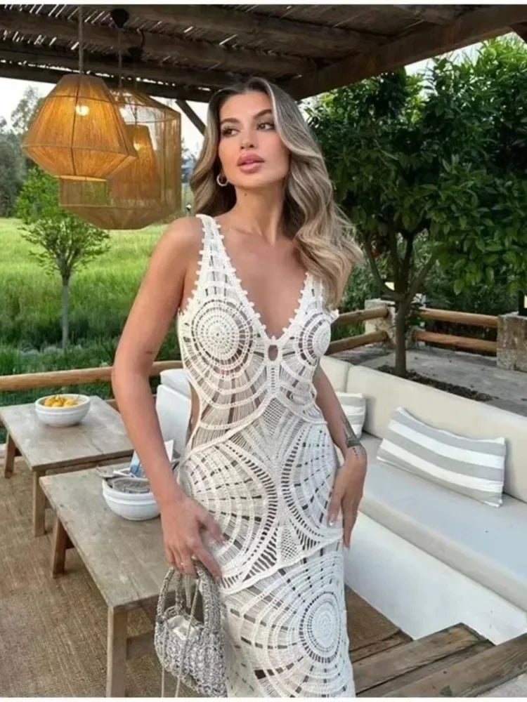 Woman in a white crochet maxi dress posing outdoors with a lush green background.