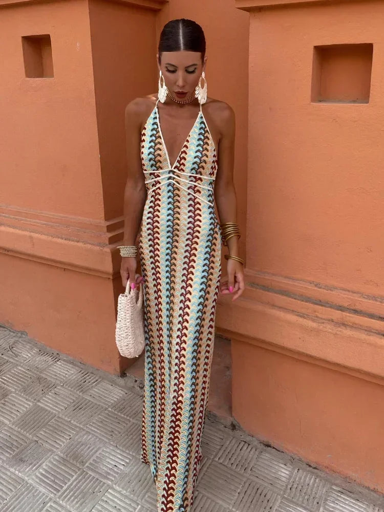 Woman wearing a long, colorful, crocheted halter dress with a geometric pattern, standing against an orange wall.