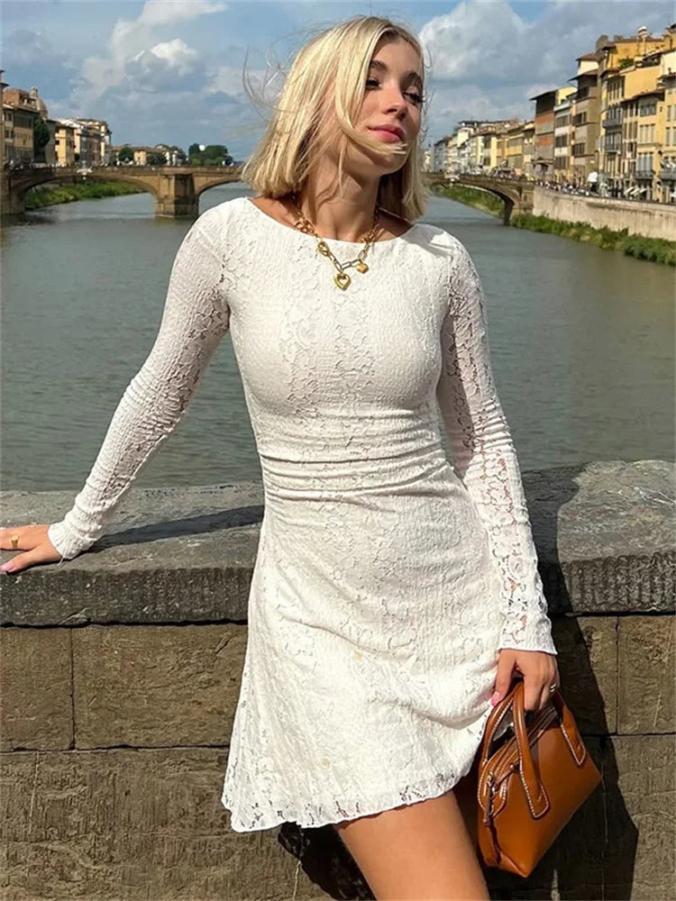 Woman in a white lace dress standing on a bridge with a river and buildings in the background.
