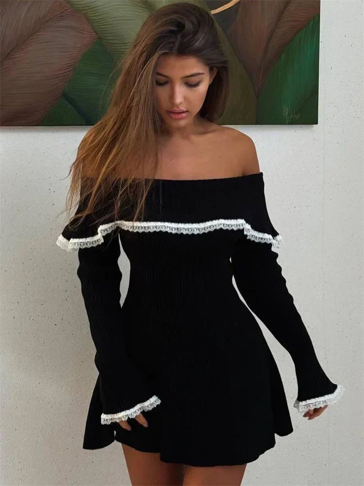A woman with long brown hair wearing a black off-the-shoulder ribbed knit dress with white lace trim.