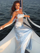 Woman in a light blue satin slip dress with a ruched bust and sheer midsection, leaning on the railing of a boat with the American flag behind her.