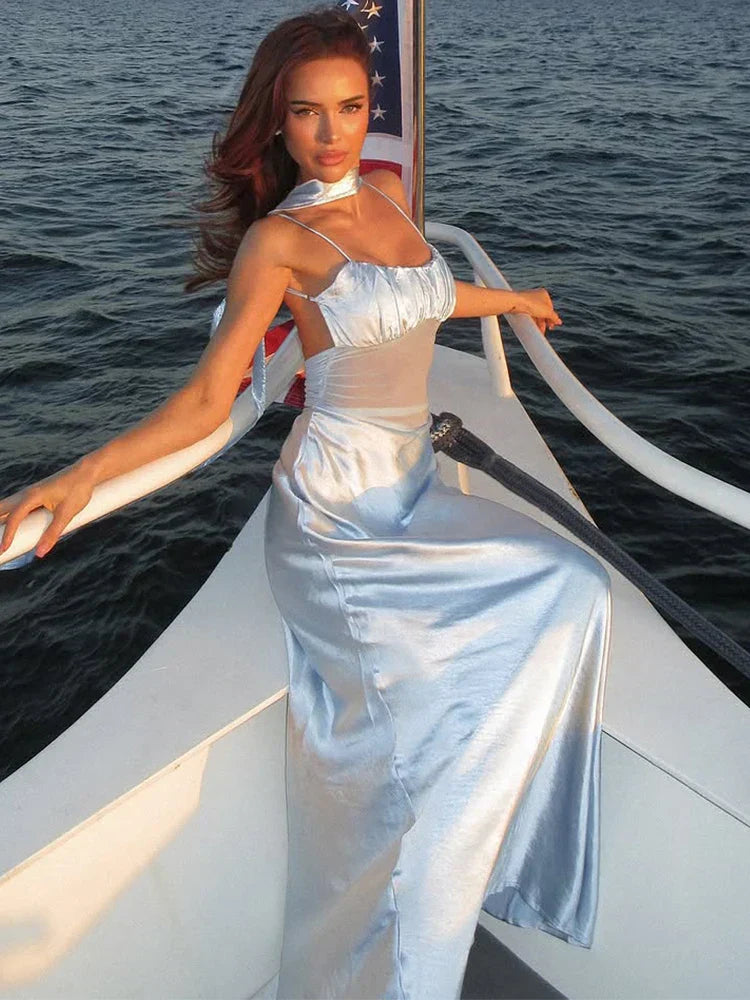Woman in a light blue satin slip dress with a ruched bust and sheer midsection, leaning on the railing of a boat with the American flag behind her.