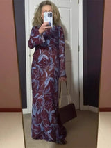 Woman in a sheer burgundy and blue floral print maxi dress, holding a handbag and taking a mirror selfie.