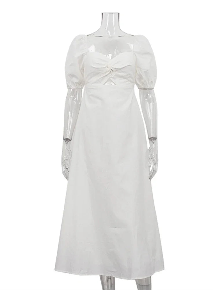 A white midi dress with puff sleeves, a sweetheart neckline with a twist front detail, and a cut-out at the waist, displayed on a mannequin.