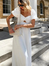 Woman adjusting her white quilted handbag while wearing a white puff sleeve midi dress with a cut-out detail and twist front bodice.