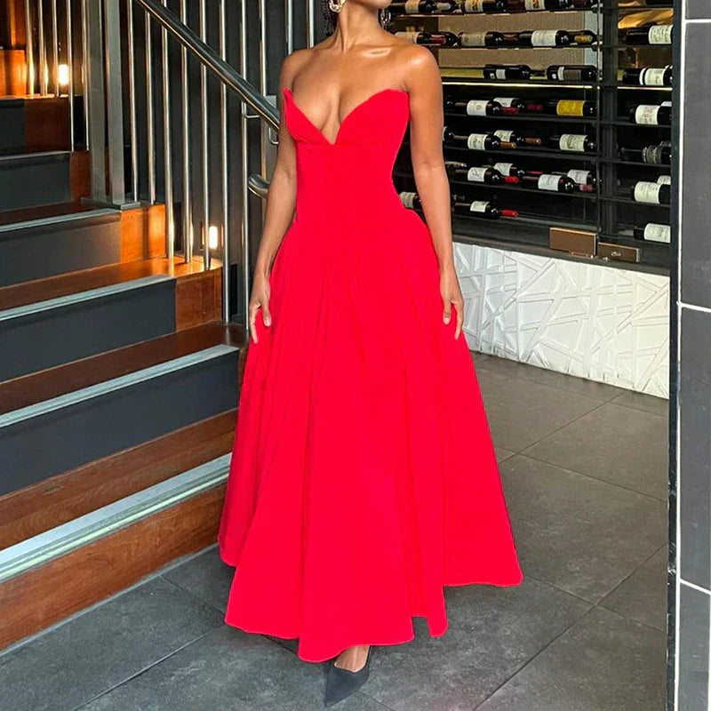 Woman in a red satin strapless dress with a full skirt, standing near a staircase and wine racks.