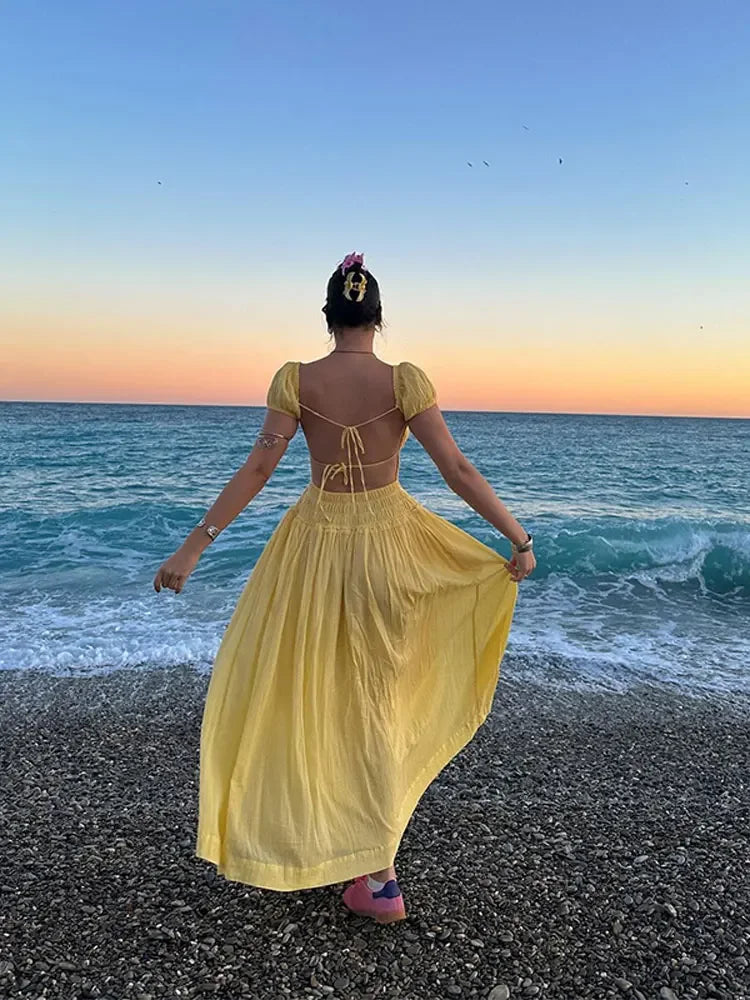 Woman in a yellow dress standing on a beach at sunset