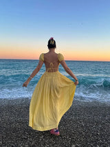 Woman in a yellow dress standing on a beach at sunset