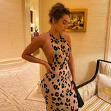 Woman in a beige and black leopard print halter dress with a low back, standing in a hallway.