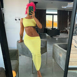 Woman with bright pink hair in a yellow two-piece set with a cropped top and a high-waisted, ruched skirt with a side cut-out, posing in a modern living room.