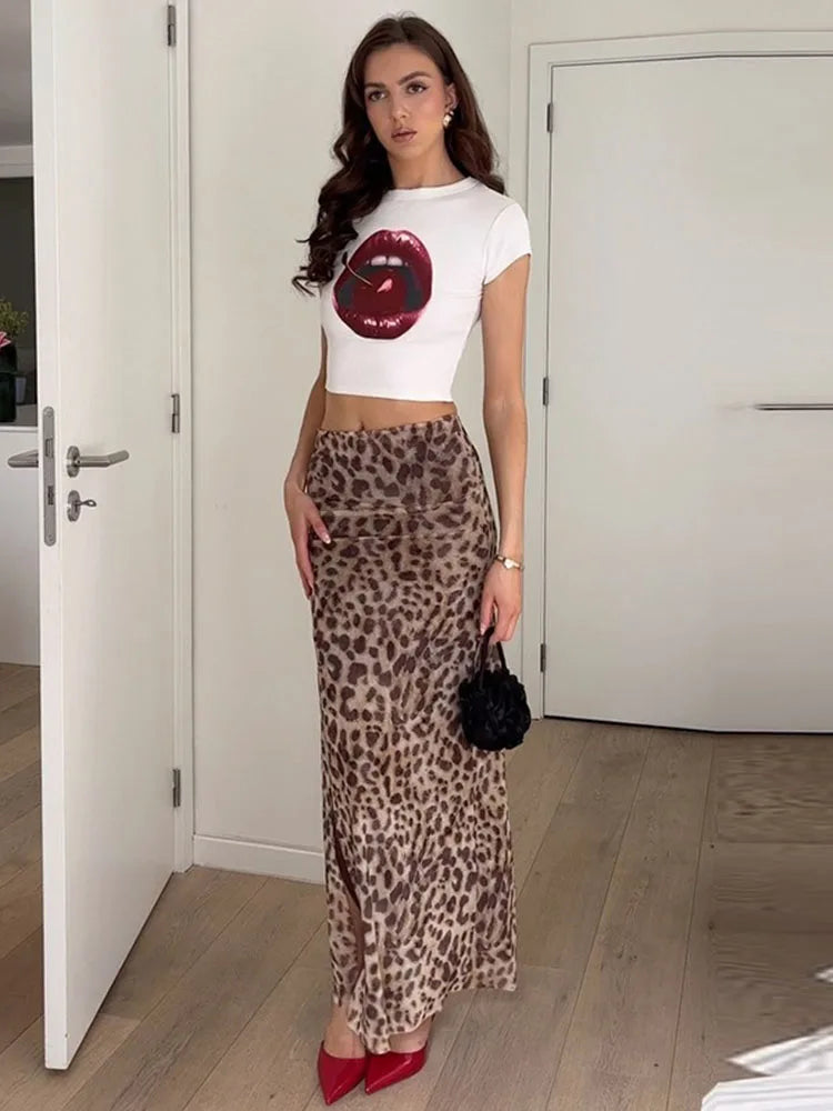 A woman wearing a white crop top with a cherry graphic and a long leopard print skirt.