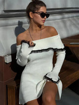 A woman in sunglasses wearing a white off-the-shoulder ribbed knit dress with black lace trim, looking to the side.