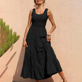 Woman wearing a black tiered maxi dress with a smocked bodice, standing against a pink wall with a cactus.