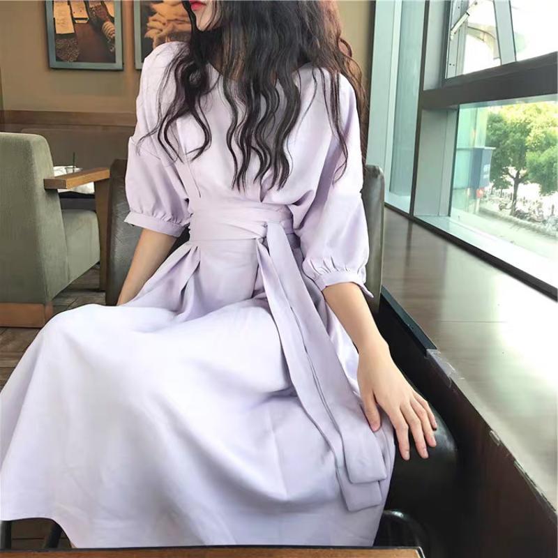 A woman sits in a cafe wearing a lavender midi dress with a tie waist and puff sleeves.