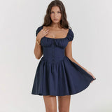A woman wearing a navy blue short dress with puffy sleeves and a corset bodice, touching her necklace.