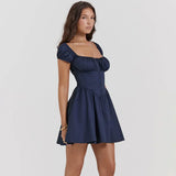 A woman wearing a navy blue short dress with puffy sleeves and a corset bodice, shown from the side with her hand on her hip.