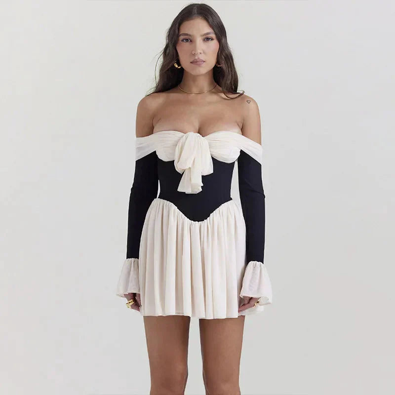 woman in a black and white off-the-shoulder dress with a bow detail and flared sleeves, posing