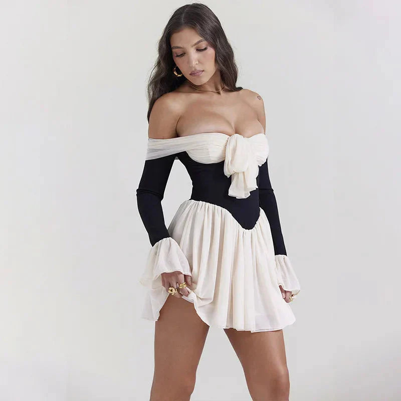 woman lifting the hem of a black and white off-the-shoulder dress with a bow detail and flared sleeves