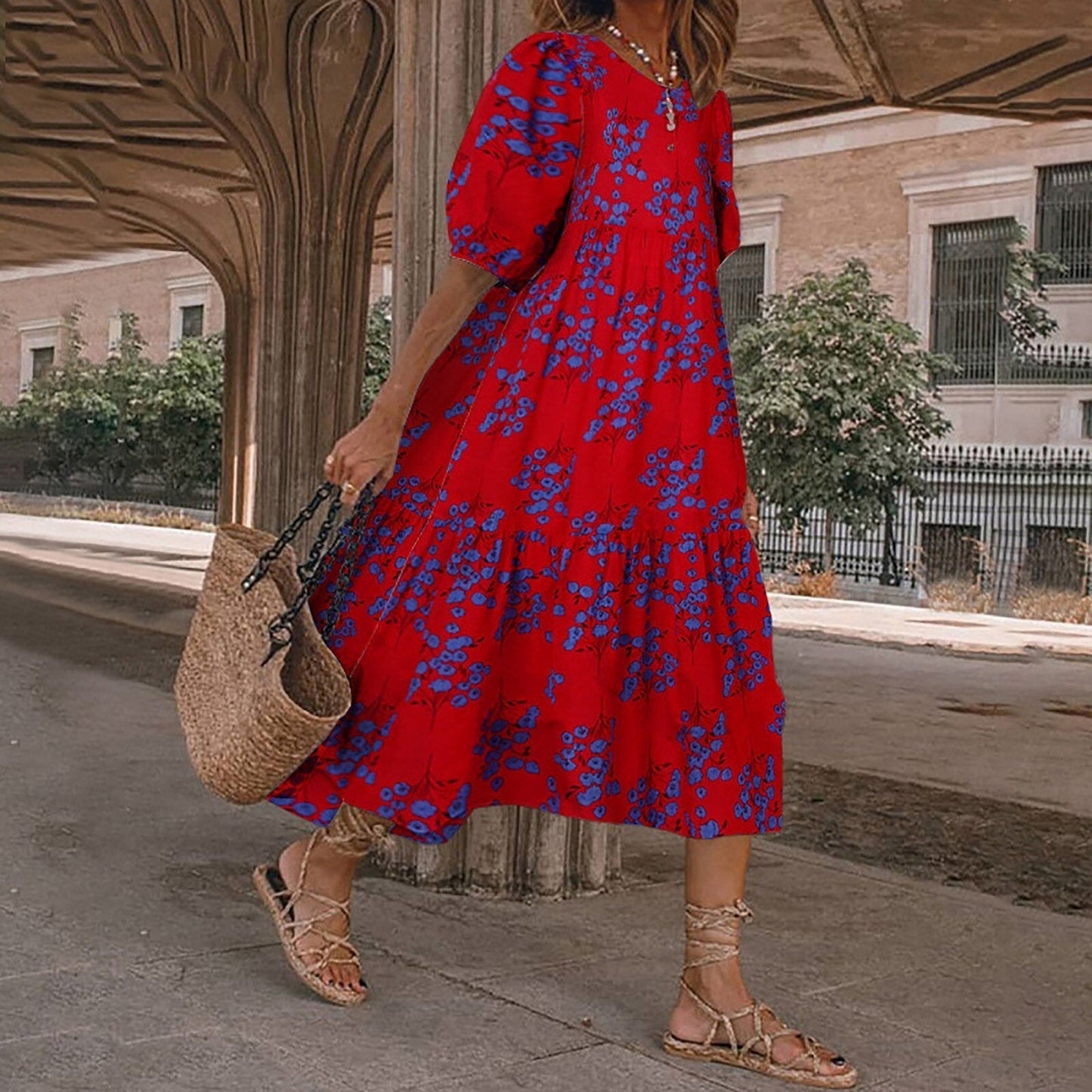 A woman wearing a red midi dress with a blue floral print and puff sleeves, carrying a straw bag.