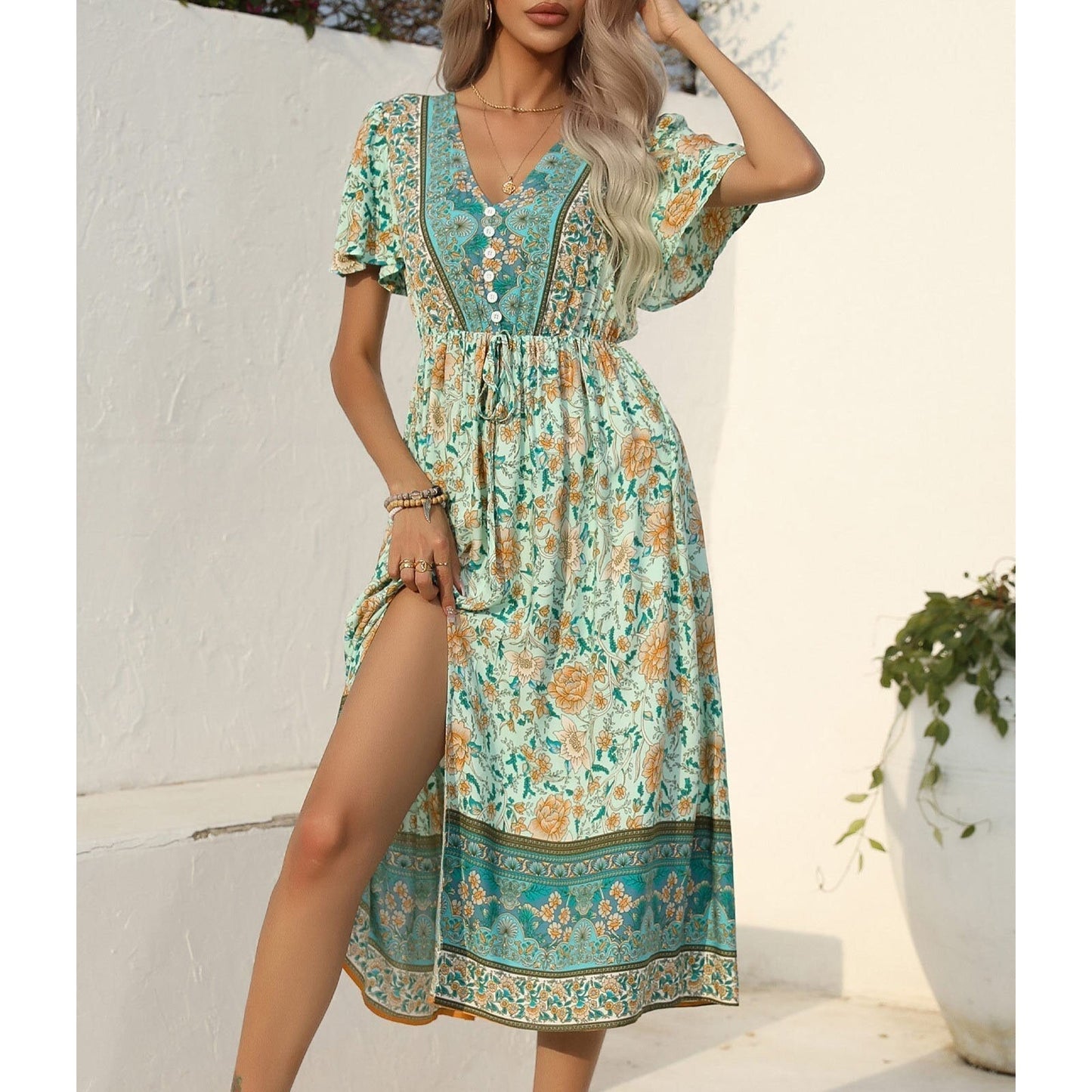 Woman wearing a green and orange floral midi dress with a high slit.