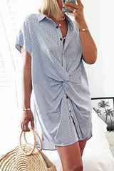 A woman in a blue and white striped shirt dress with a twist knot, holding a straw bag and a phone.