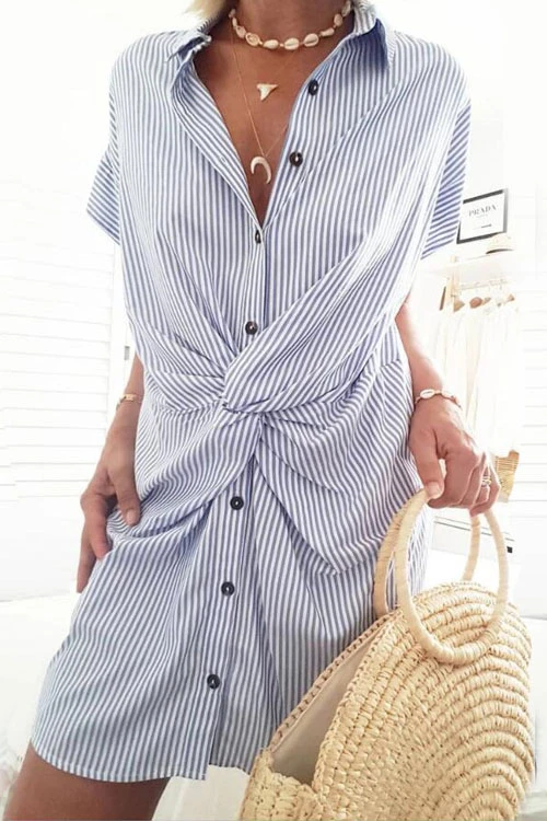 A woman wearing a blue and white striped shirt dress with a twist knot detail at the waist, holding a straw bag.