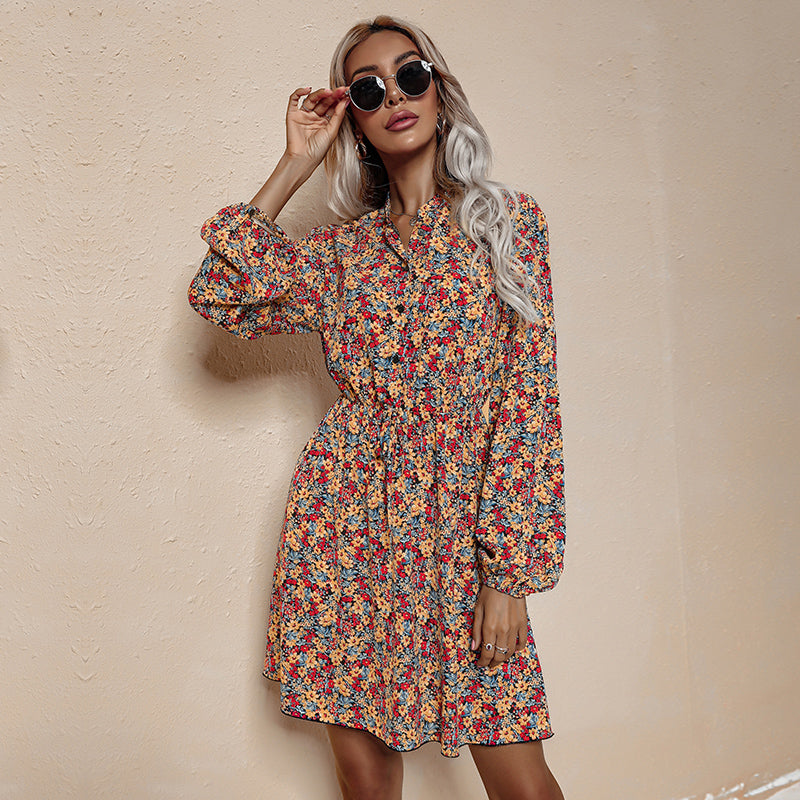 A woman models a yellow floral print dress with long bishop sleeves and a v-neck.