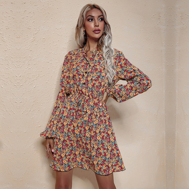 A woman poses in a yellow floral print dress with a cinched waist and button-down neckline.
